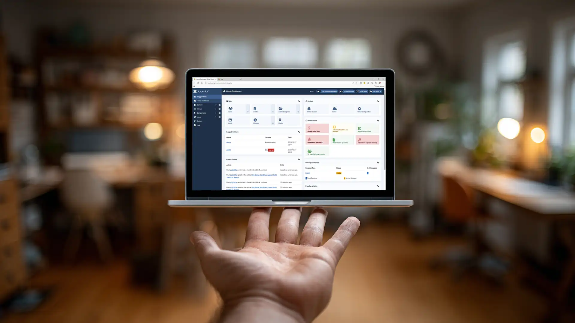 A close up of a hand holding a miniature laptop with a screenshot of the Joomla dashboard